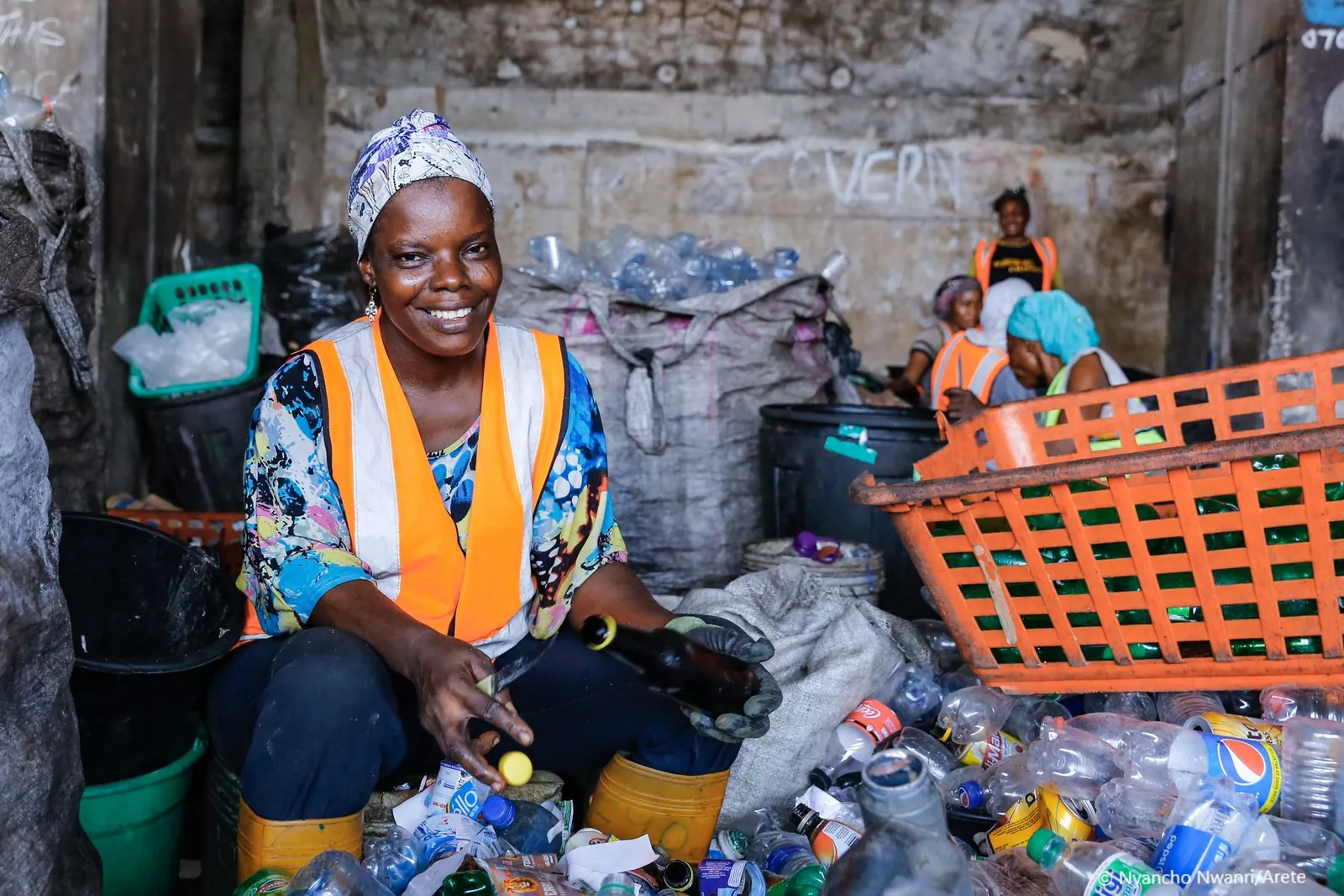 A woman collector smiling while sorting recovered plastic bottles at a community hub