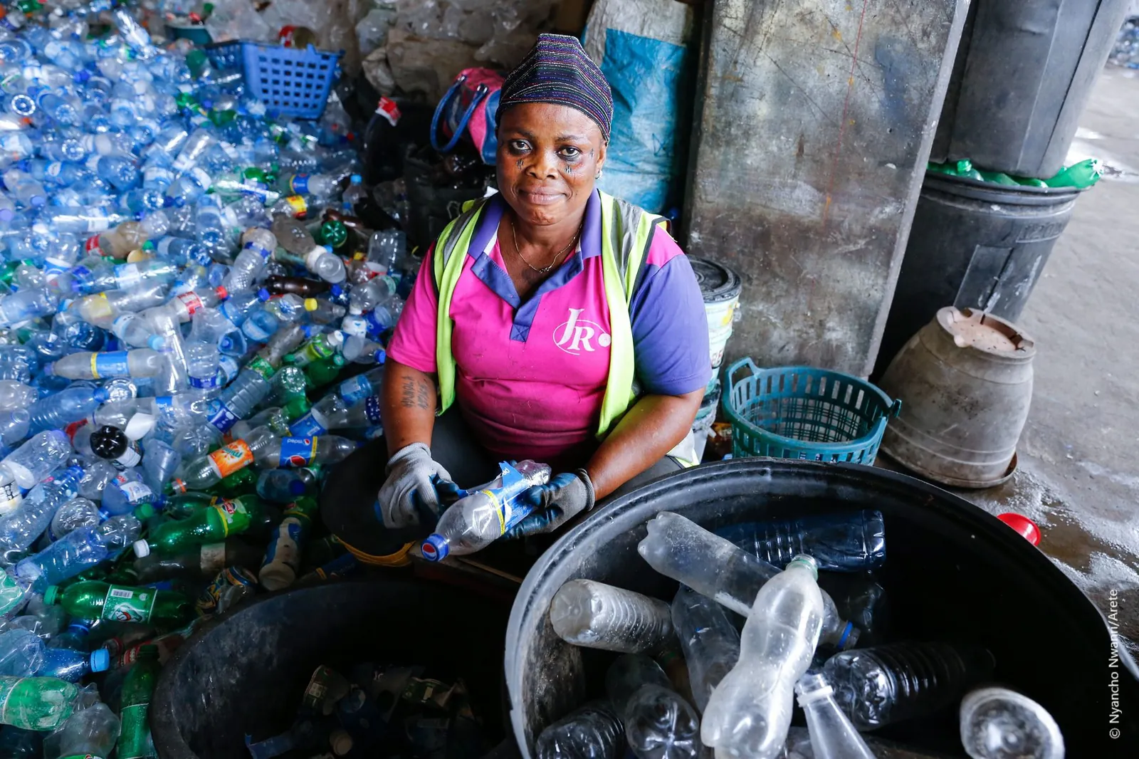 A woman collector in high-visibility gear sorting recovered plastic bottles